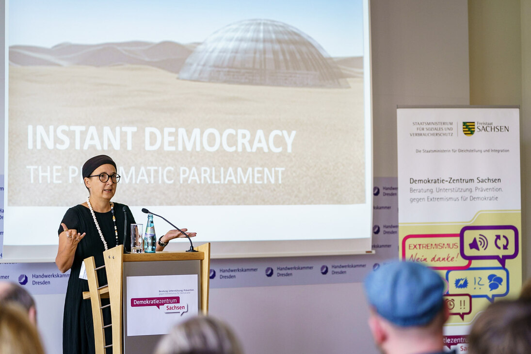 Frau Prof. Besand während ihres Vortrags »Politische Bildung für alle?!«. Im Hintergrund ist per PowerPoint-Präsentation eine Art Kuppel zu sehen und der Schriftzug Instant Demokratie.