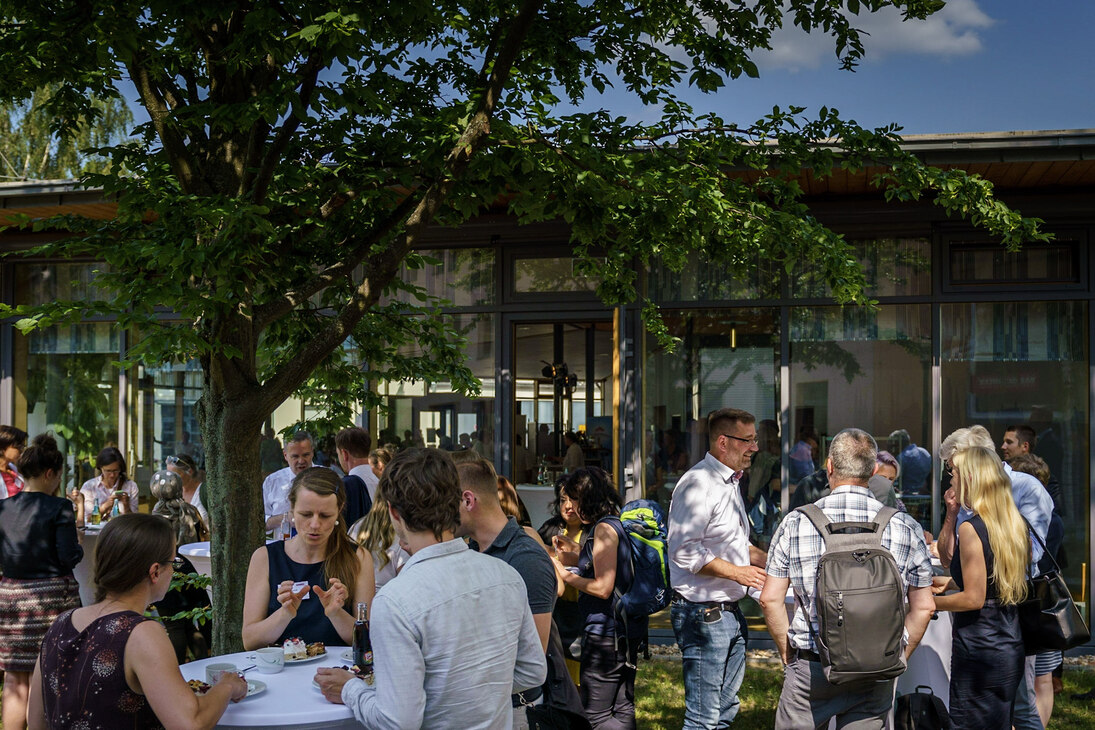 Netzwerken im Garten der Handwerkskammer Dresden. An zahlreichen Tischen stehen kleinere Gruppen der Teilnehmenden.