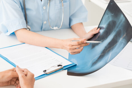 Mediziner führt Aufklärungsgespräch und hält dabei ein Röntgenbild von einer Lunge in der Hand