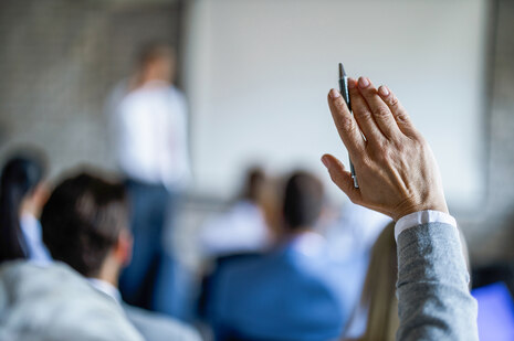 Ein Zuhörer hebt bei einer Veranstaltung bzw. bei einem Vortrag seine rechte Hand, um sich zu Wort melden zu können