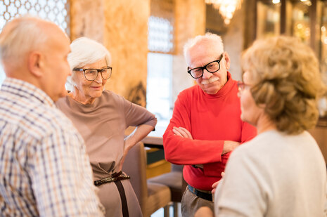 Eine im Kreis stehende Gruppe von zwei älteren Damen und zwei älteren Herren im Gespräch