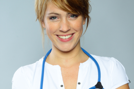 Eine junge Ärztin lächelt in die Kamera. Sie trägt ein Stetoskop um den Hals.