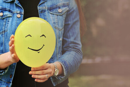 Frau hält Luftballon mit aufgemaltem Smiley in die Kamera